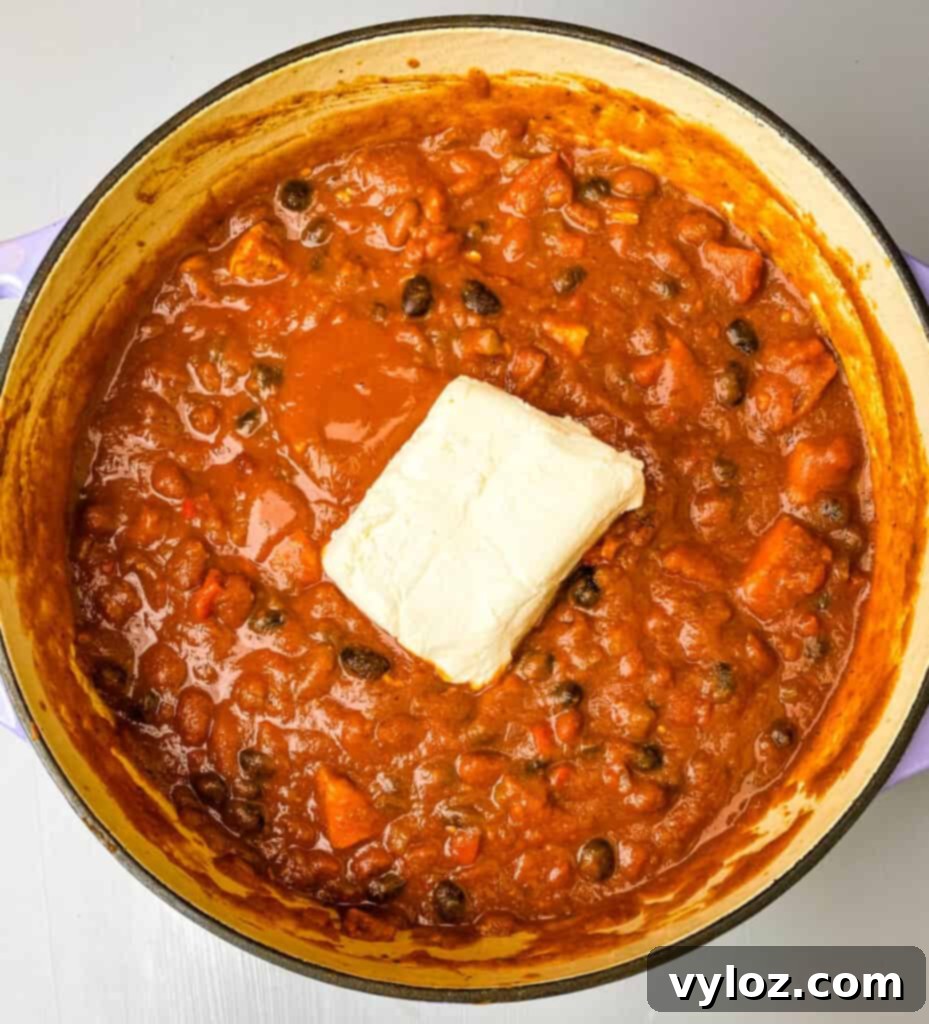 Autumnal Pumpkin Chicken Chili 7 A creamy Pumpkin Chicken Chili in a Dutch oven, with swirls of melted cream cheese beautifully incorporated into the rich, orange-hued mixture.