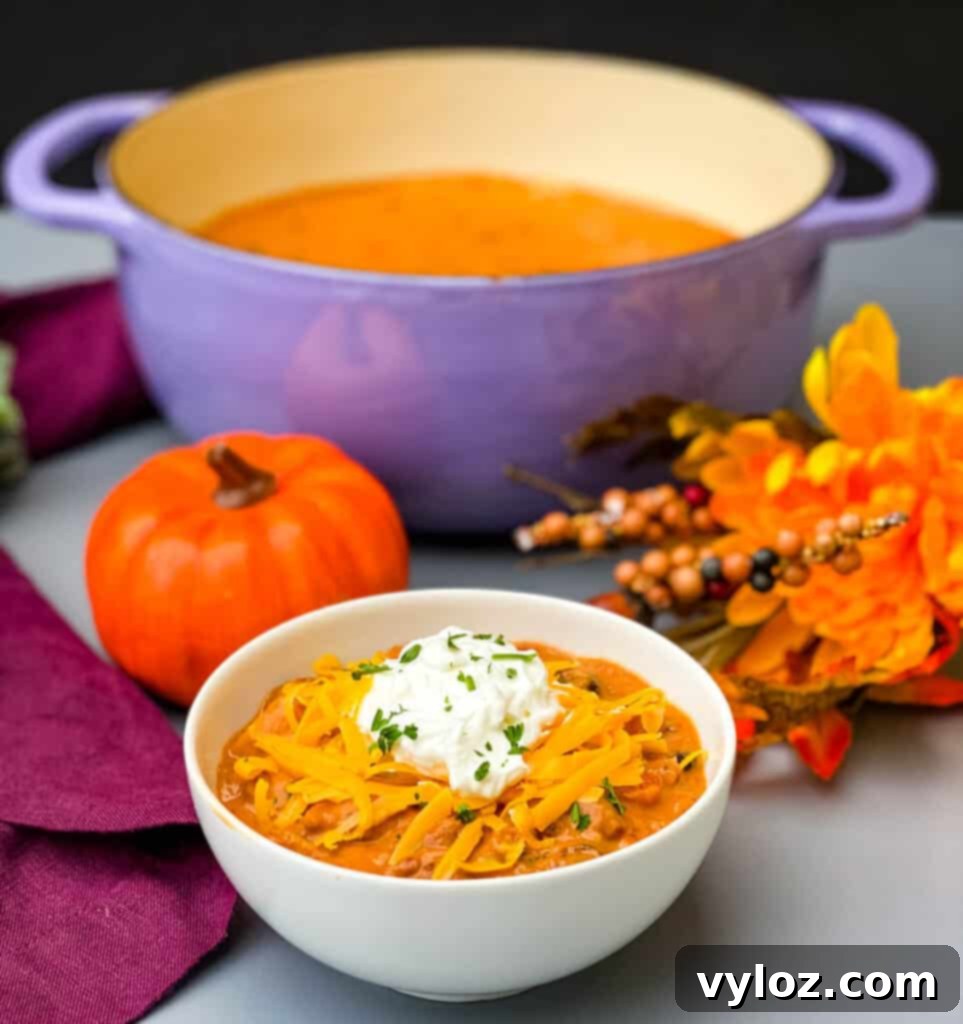 Autumnal Pumpkin Chicken Chili 9 A beautifully presented bowl of Pumpkin Chicken Chili, accompanied by a matching purple Dutch oven filled with more chili, evoking a warm and inviting autumn meal scene.