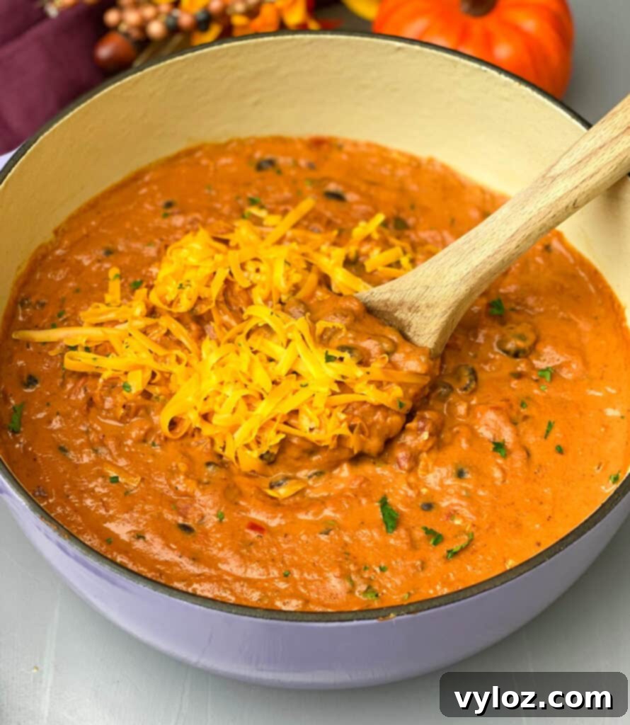 Autumnal Pumpkin Chicken Chili 10 Two bowls of pumpkin chicken chili, one garnished with shredded cheese, with a purple Dutch oven in the background, highlighting various serving options.