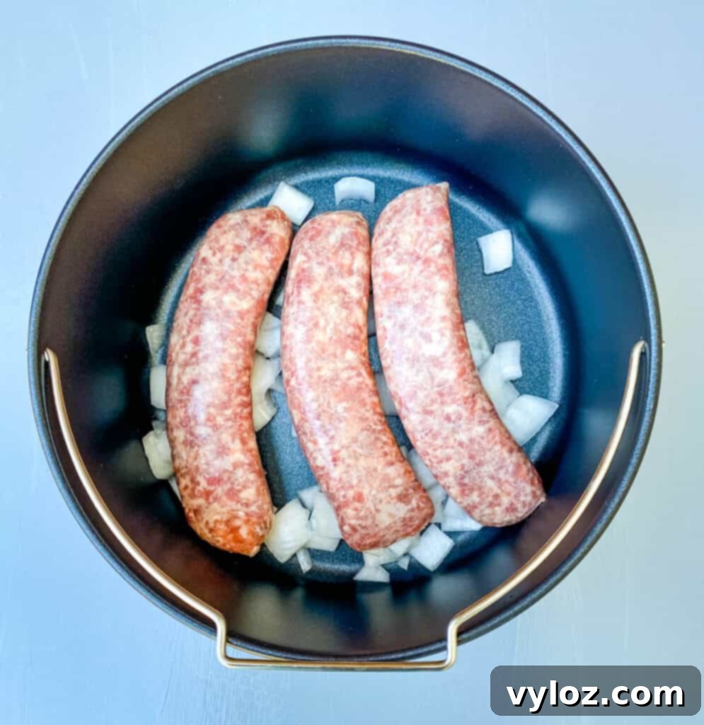 brats cooking in an air fryer with sliced onions