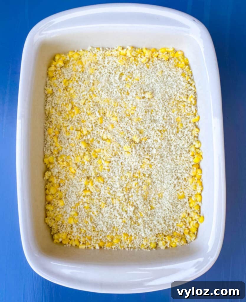 Uncooked scalloped corn mixture evenly spread in a baking dish, topped with breadcrumbs, ready for the oven.