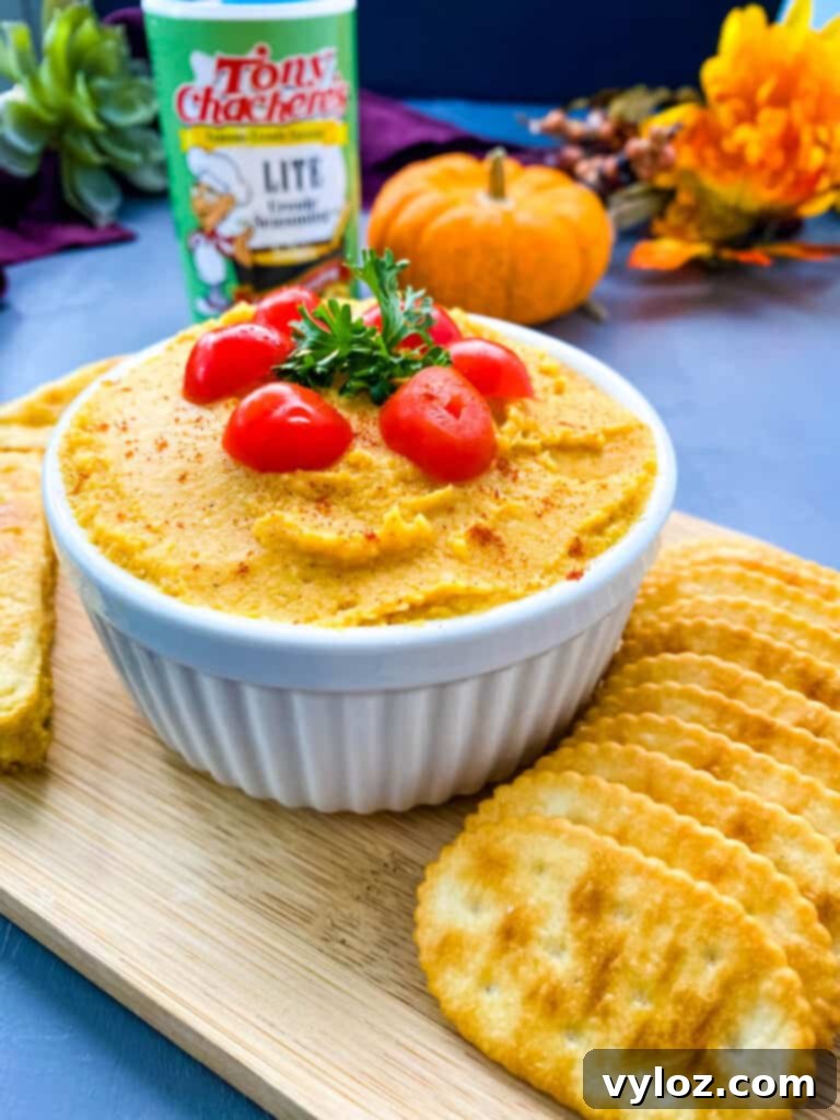 Creamy pumpkin hummus served on a plate with an assortment of crispy crackers and savory cornbread triangles, perfect for dipping.
