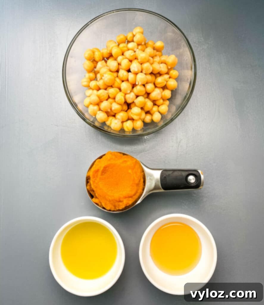 Separate bowls containing key ingredients: plump chickpeas, smooth pureed pumpkin, golden olive oil, and sweet honey, ready for blending into delicious hummus.