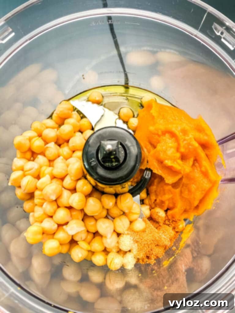 Unblended pureed pumpkin, chickpeas, and spices in a food processor bowl, ready to be transformed into hummus.