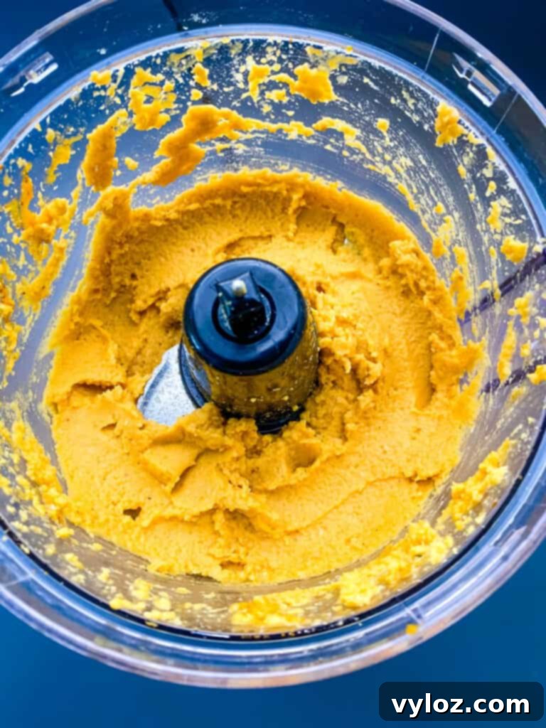 Smooth and creamy pumpkin hummus fully blended in a food processor, showcasing its vibrant orange color.