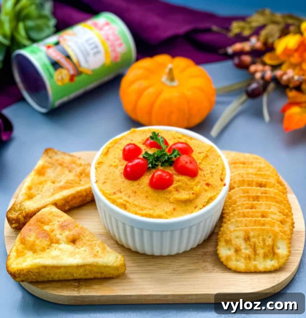 Serving board featuring a bowl of pumpkin hummus garnished with paprika, surrounded by crispy crackers and slices of golden cornbread.