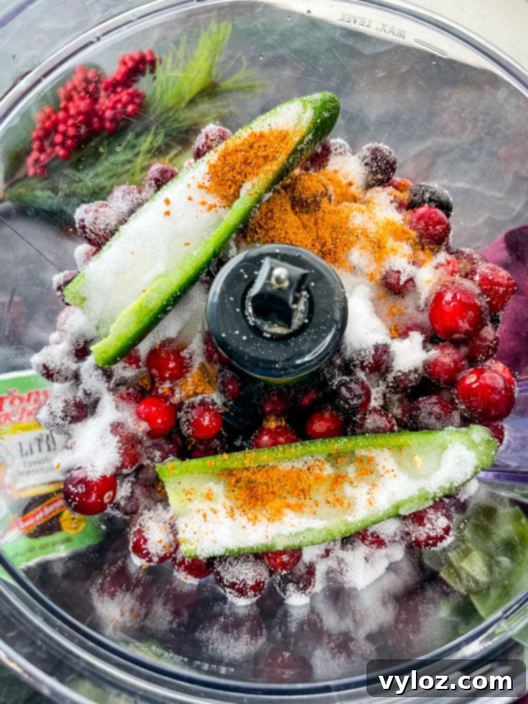 Fresh jalapeno, cranberries, and sweetener being added to a food processor for Cranberry Jalapeno Dip preparation.