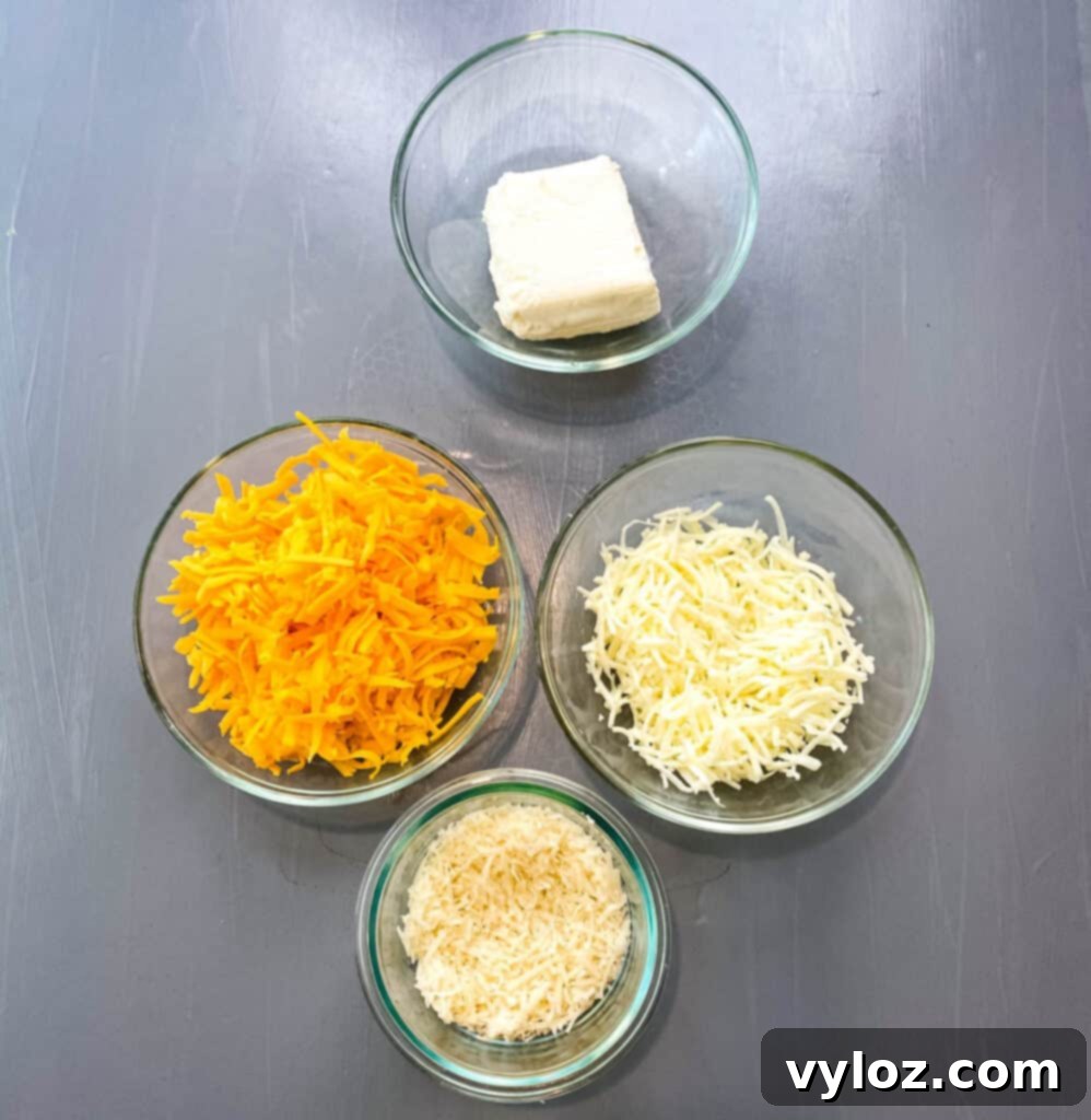 cream cheese, shredded cheddar, mozzarella, and parmesan cheese in separate glass bowls