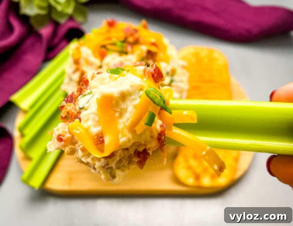 A person holding a piece of celery generously topped with Million Dollar Dip.