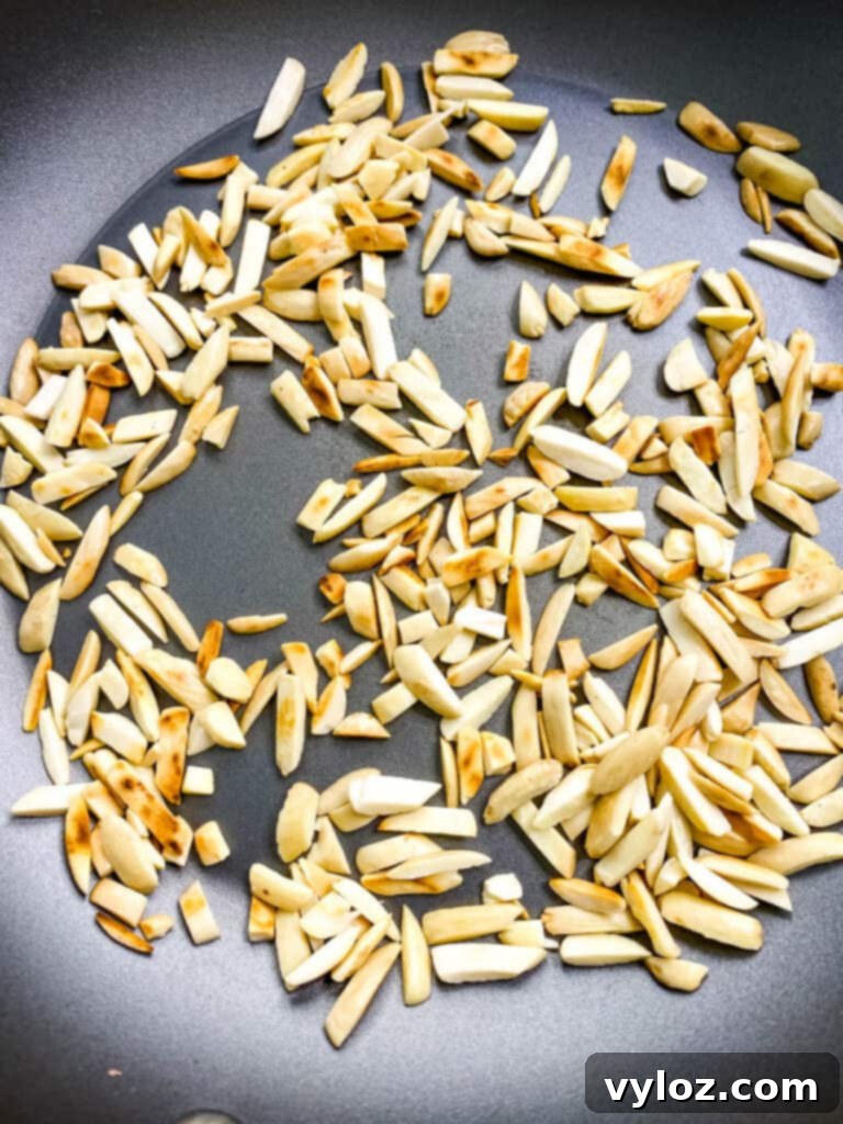 Close-up of slivered almonds toasting in a skillet, highlighting their rich, golden hue.
