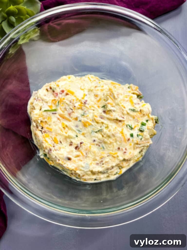 A close-up view of Million Dollar Dip in a glass bowl, highlighting the bits of bacon, cheese, and almonds.