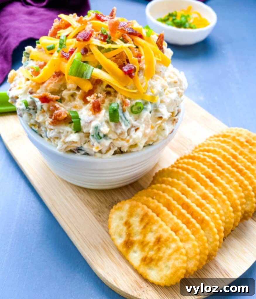 A beautifully presented white bowl of Million Dollar Dip, garnished with crackers and celery for dipping.