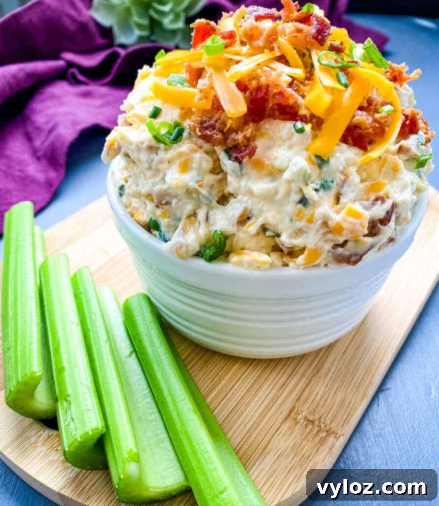 A large white bowl filled with Million Dollar Dip, beautifully garnished with crackers and celery sticks.