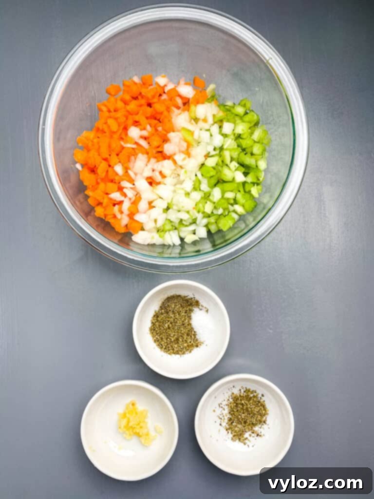 Chopped onions, carrots, and celery in a glass bowl, alongside minced garlic and Italian seasoning – the aromatic foundation of the soup.