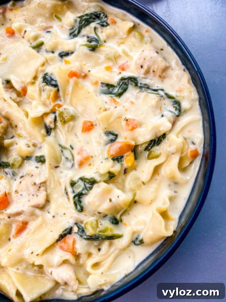 A beautifully presented bowl of Creamy Chicken Lasagna Soup, garnished with fresh basil leaves and a sprinkle of Parmesan, in a vibrant blue bowl.