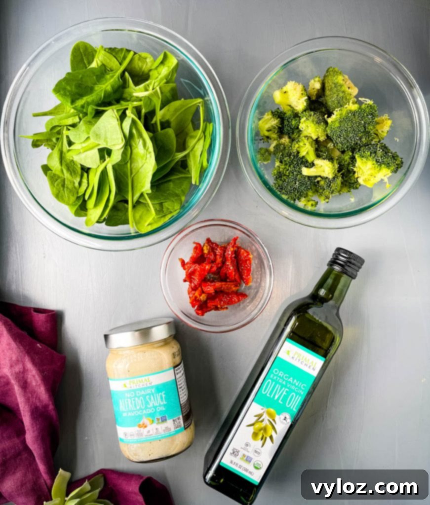 fresh spinach, fresh broccoli, sundried tomatoes, primal kitchen alfredo, and primal kitchen olive oil on a flat surface
