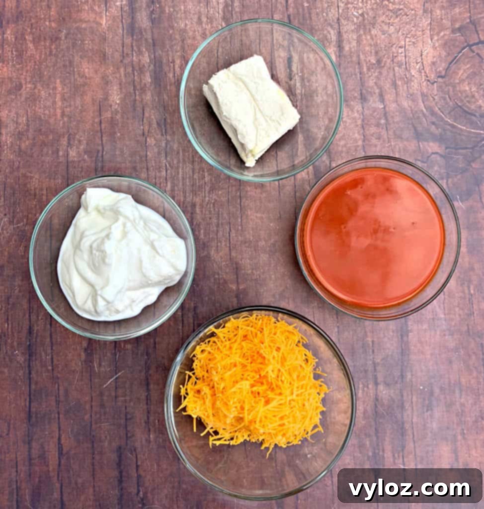 Selection of key ingredients including cream cheese, buffalo sauce, and shredded cheese for making buffalo chicken dip.