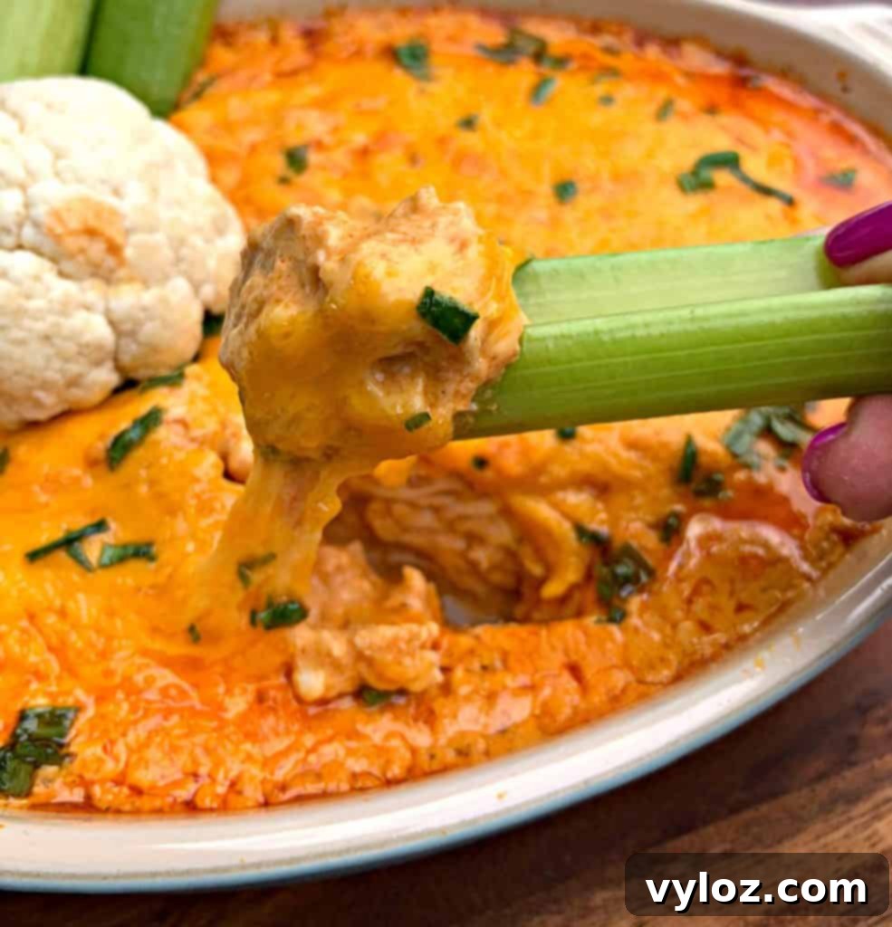 Person scooping keto low carb buffalo chicken dip with a celery stick, showing its creamy texture.