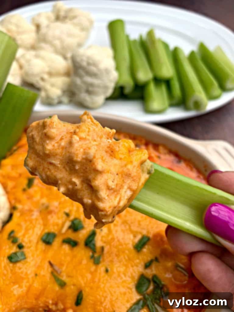 A bowl of keto low carb buffalo chicken dip garnished with green onions and surrounded by celery sticks.