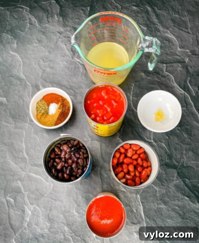 broth, black beans, kidney beans, chili seasoning, tomato sauce petite tomatoes, and garlic in separate bowls on a flat surface