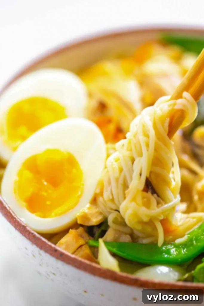 A close-up of Instant Pot chicken ramen being lifted from a bowl with chopsticks, showing the noodles and chicken.