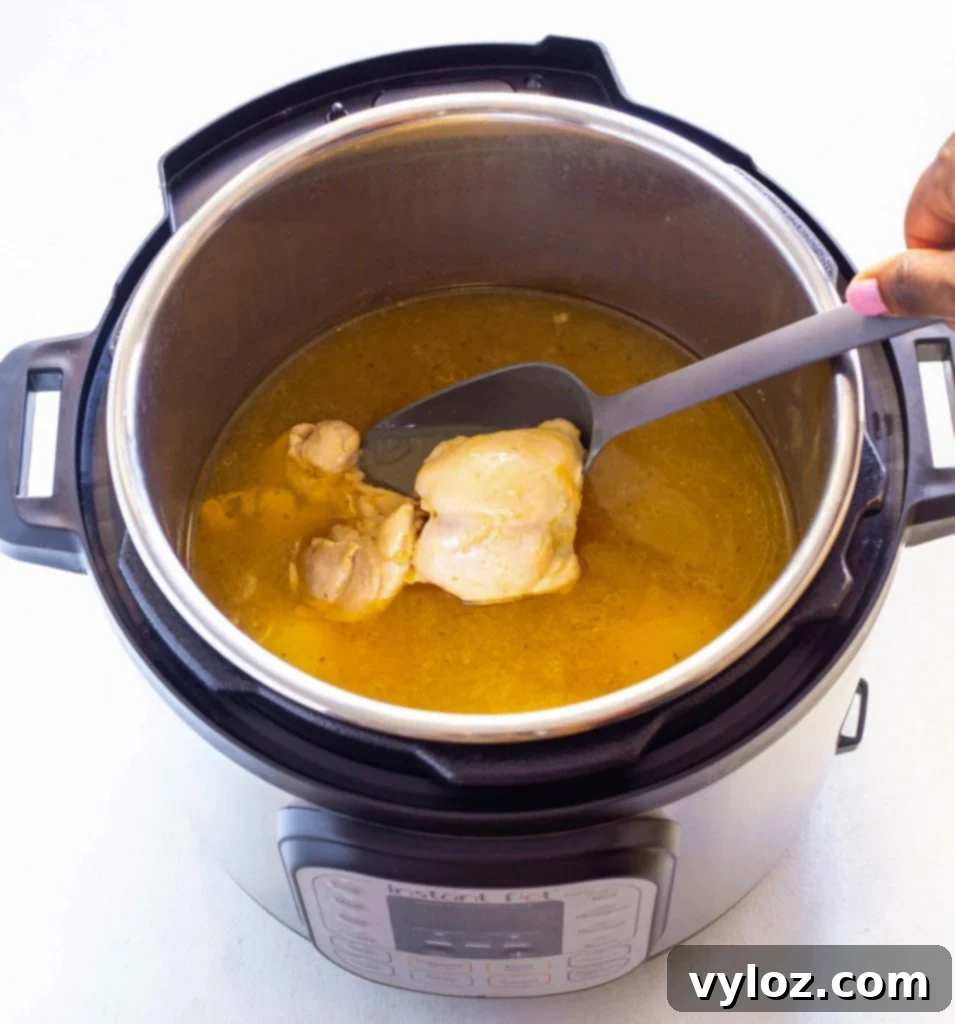 Cooked chicken thighs in an Instant Pot with simmering broth, ready for the next step of adding vegetables.