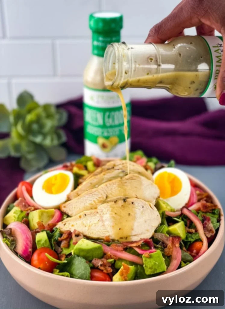 Green Goddess dressing being drizzled over the colorful Cobb salad ingredients