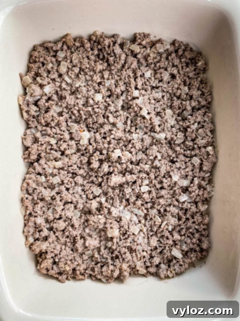 Big Mac Bake 7 Cooked ground beef mixture spread evenly in a ceramic casserole dish, forming the base of the Big Mac Casserole before adding other layers.