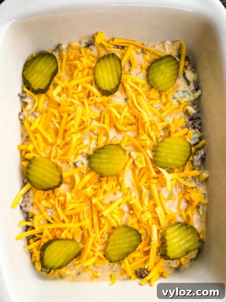 Big Mac Bake 10 The Big Mac Casserole assembly process, showing the ground beef, sauce, and cheese layers, and finally topped with more shredded cheddar cheese and optional pickle slices.