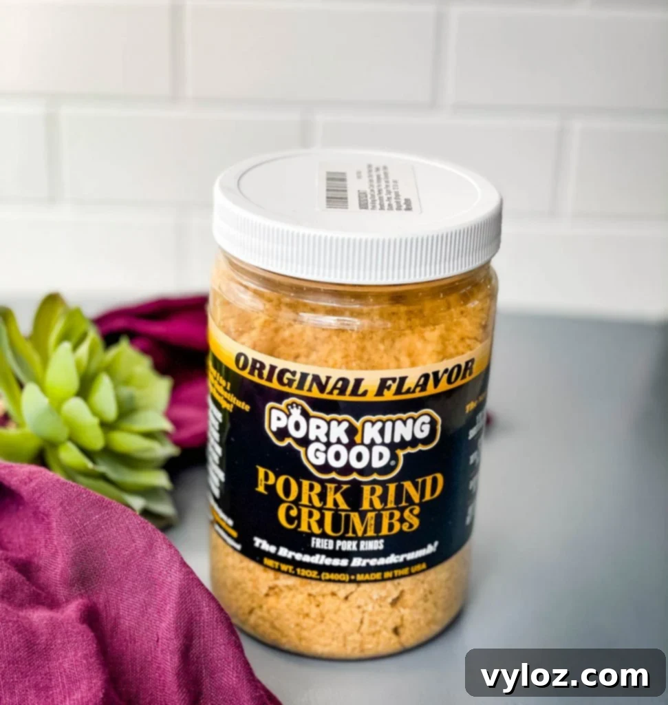 Crispy Keto Low-Carb Onion Rings 5 Finely crushed pork rinds, a crucial keto-friendly breading ingredient, are shown in a transparent container on a flat surface, ready for preparing crispy onion rings.