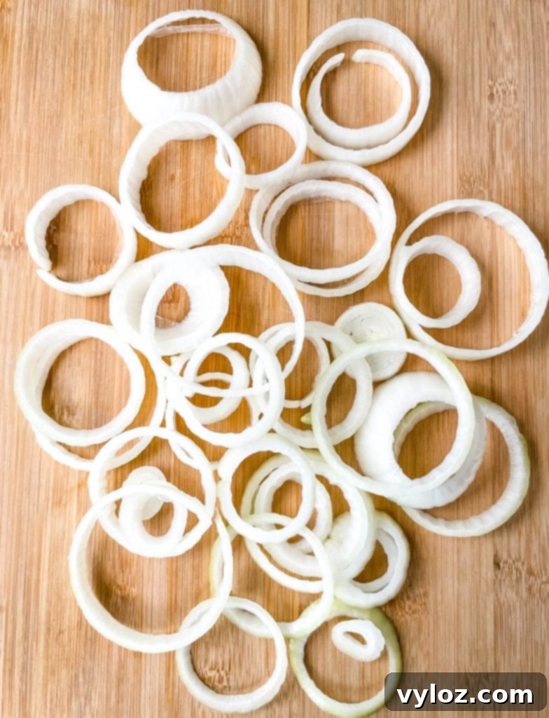 Crispy Keto Low-Carb Onion Rings 6 Freshly sliced raw onion rings arranged neatly on a bamboo cutting board, showcasing their perfect thickness before breading.