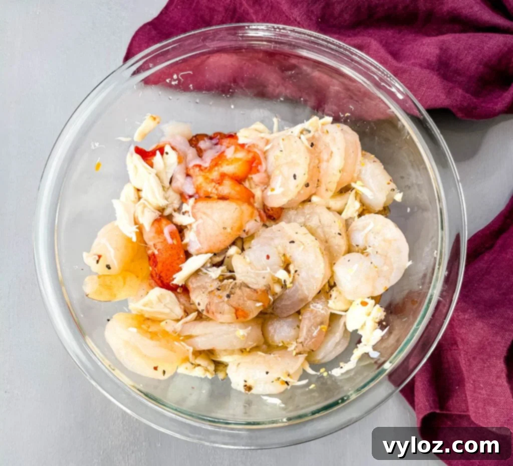Raw, uncooked shrimp, lobster, and crab meat in a clear glass bowl, showcasing their fresh appearance before being added to the chili.