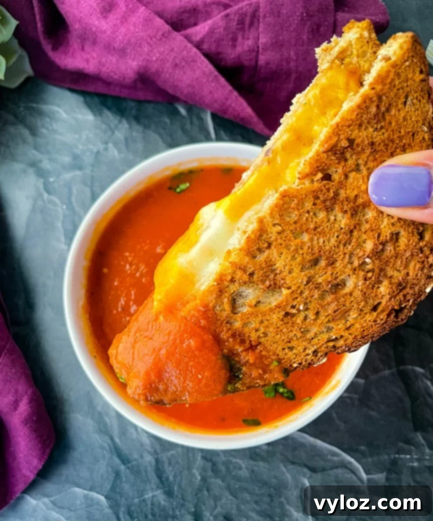Person holding a grilled cheese sandwich over tomato soup