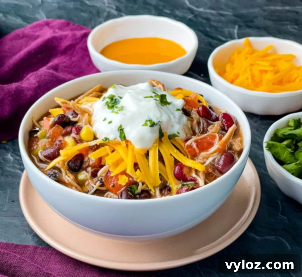 Tangy Buffalo Chicken Chili 2 A generously portioned white bowl of buffalo chicken chili, adorned with a sprinkle of shredded cheese and a dollop of cooling sour cream on top.