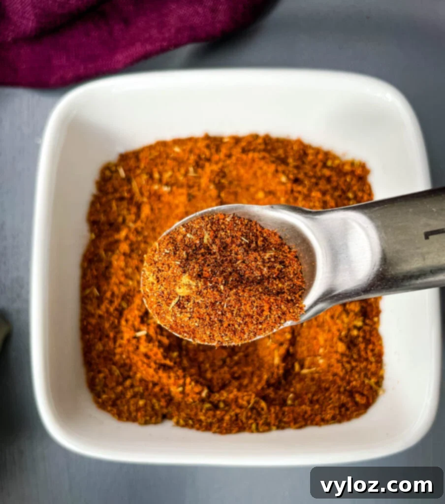 DIY Chili Spice Blend 6 Homemade chili seasoning in a white bowl with a spoon, highlighting its texture and readiness for use.