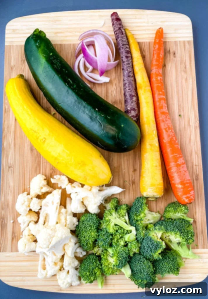 An array of fresh vegetables including squash, zucchini, onions, carrots, broccoli, and cauliflower neatly arranged on a bamboo cutting board.