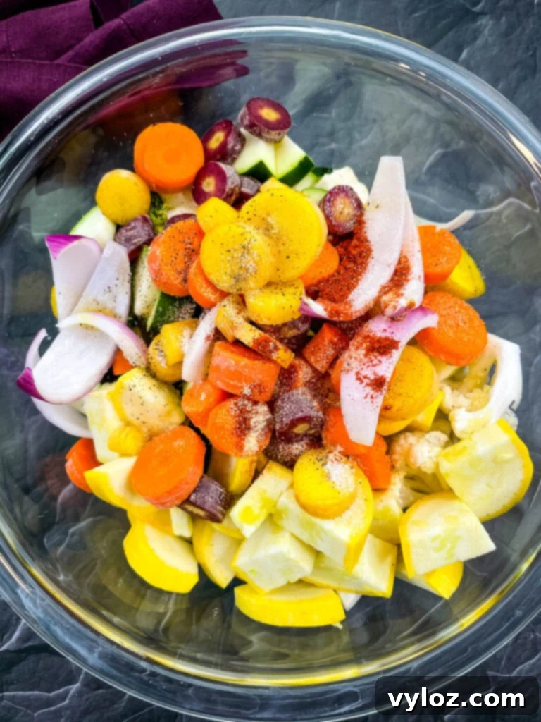 A glass bowl filled with a colorful mix of chopped zucchini, squash, red onions, carrots, broccoli, and cauliflower, glistening with marinade.