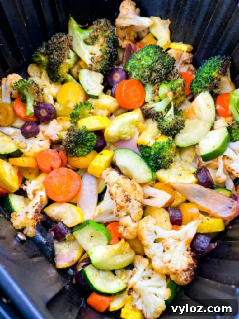 A generous serving of perfectly cooked air-fried vegetables, including squash, zucchini, onions, carrots, broccoli, and cauliflower, presented on a white plate with fresh herbs.