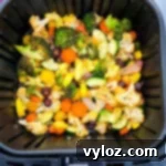 A close-up of a colorful medley of squash, zucchini, onions, carrots, broccoli, and cauliflower in an air fryer basket, showing their perfectly roasted texture.