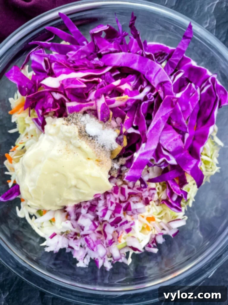 chopped red cabbage, coleslaw mix, chopped onions, mayo, and seasoning in a glass bowl