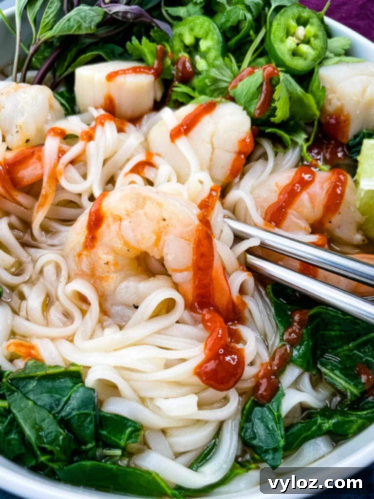 seafood shrimp pho in a white bowl drizzled with Sriracha