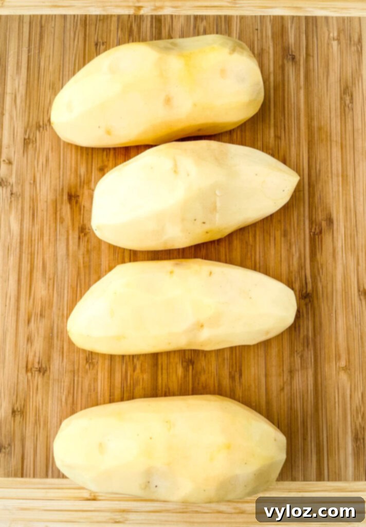 raw russet potatoes peeled on a bamboo cutting board