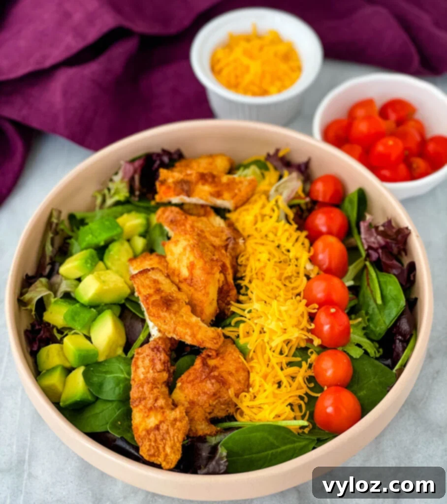 fried chicken salad in a pink bowl with avocado, tomatoes, and cheese