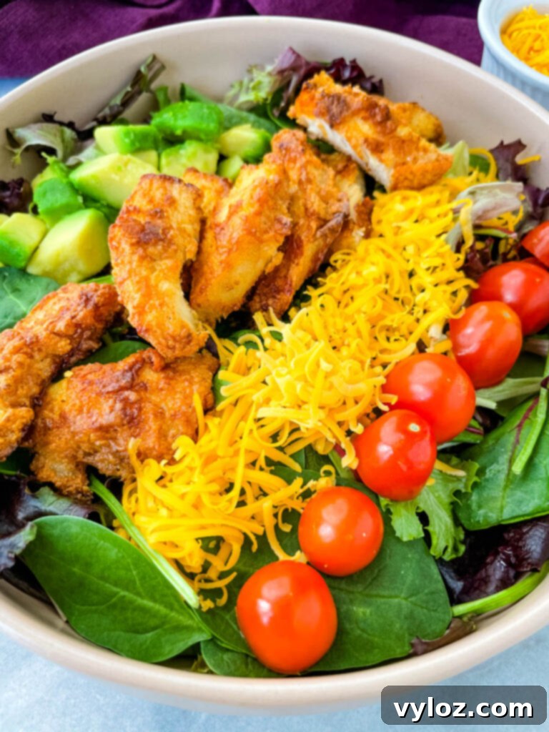 fried chicken salad in a pink bowl with avocado, tomatoes, and cheese