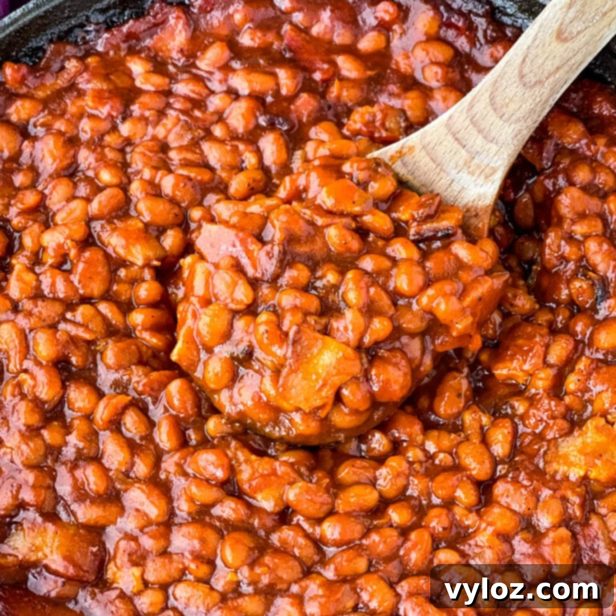 a wooden spoonful of Southern baked beans in a cast iron skillet
