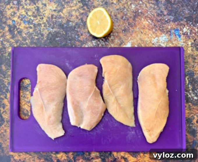 Raw chicken breasts on a purple cutting board with a fresh lemon.