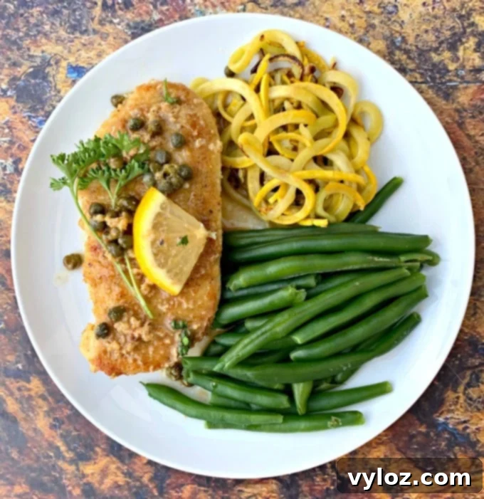Keto Lemon Chicken Piccata on a white plate with green beans and squash as side dishes.