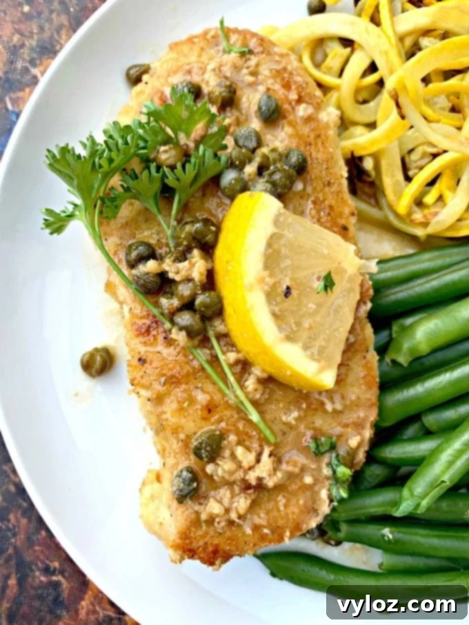 Keto Lemon Chicken Piccata on a white plate with green beans and squash, close up.