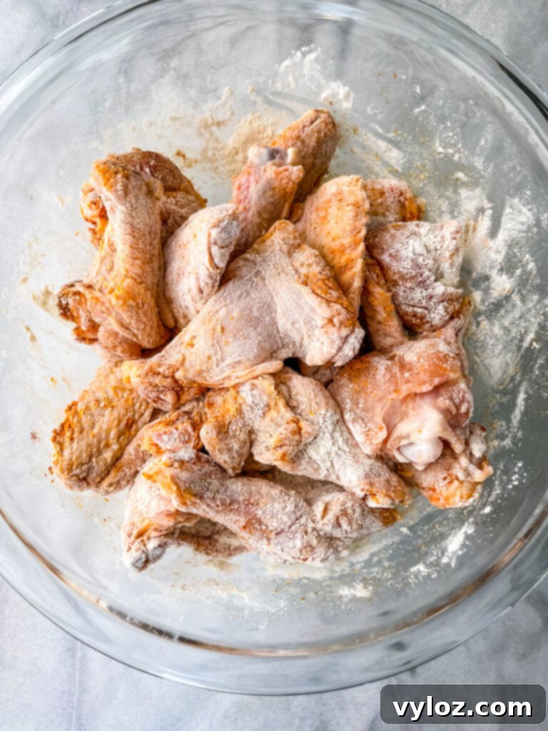 Raw, flour-dredged chicken wings waiting to be cooked, neatly arranged in a glass bowl