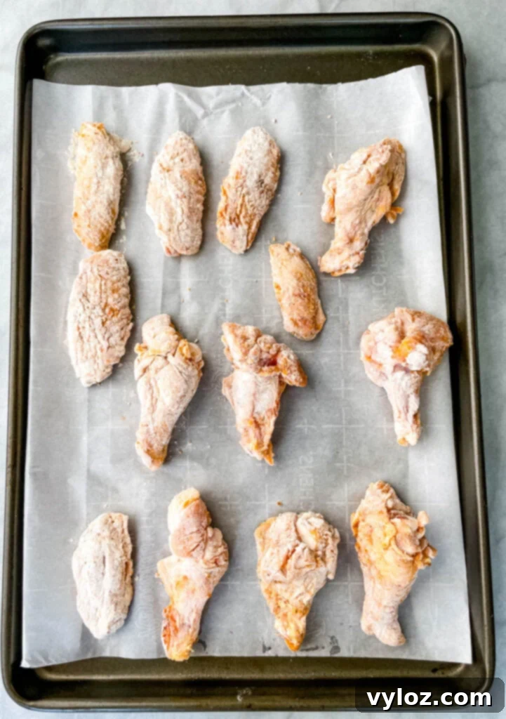 A baking sheet lined with parchment paper, holding evenly spaced, breaded chicken wings, ready for the oven